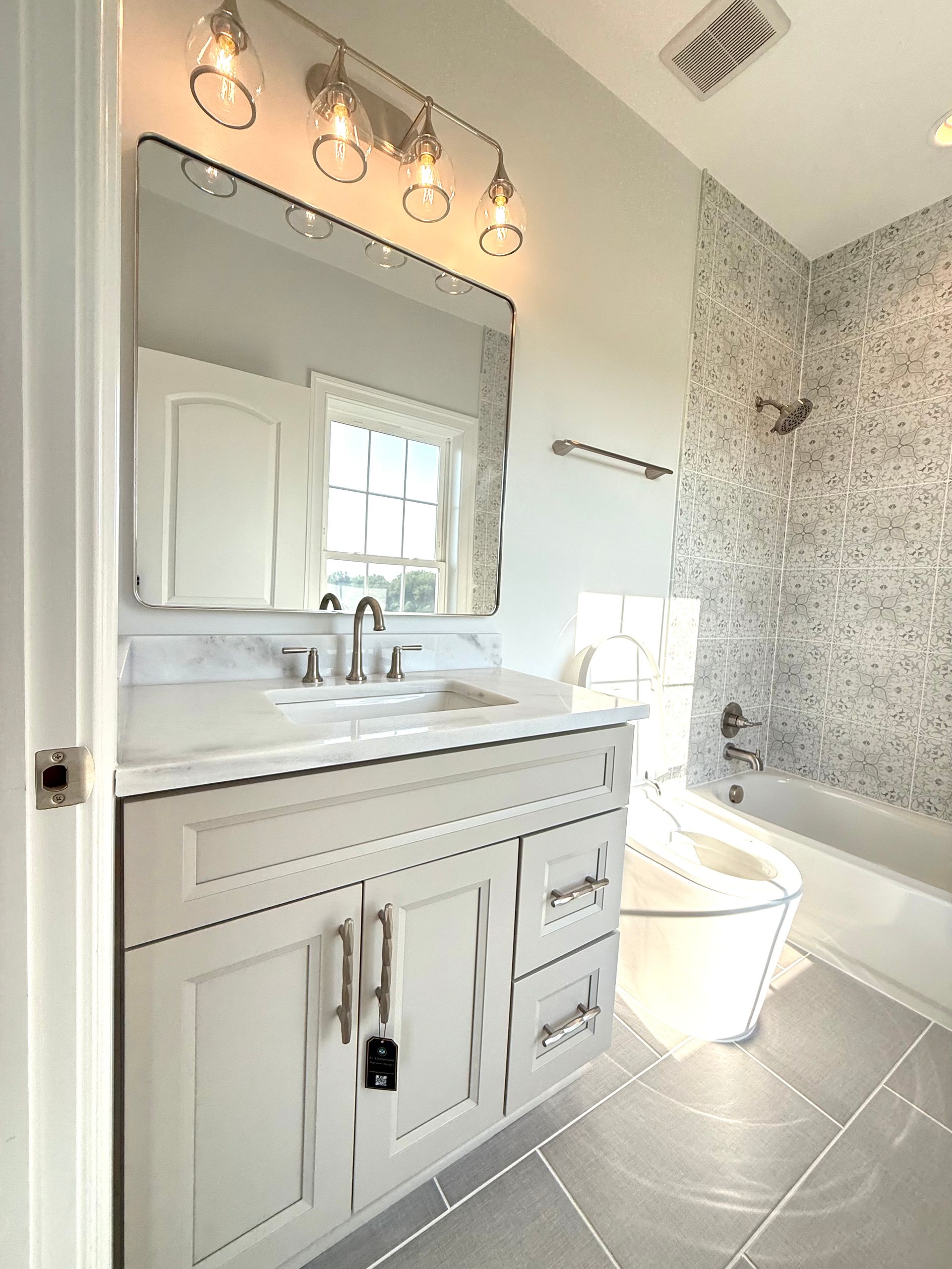 A modern, classic bathroom featuring a white tub, decorative tile, and a gray vanity with a brushed nickel faucet.