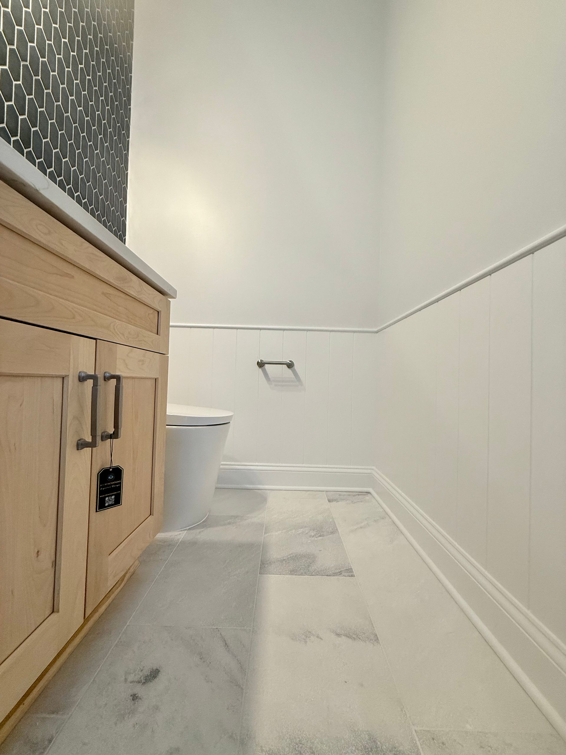 A view of a modern powder room with a natural wood vanity, a white toilet, and wainscoting on the walls.