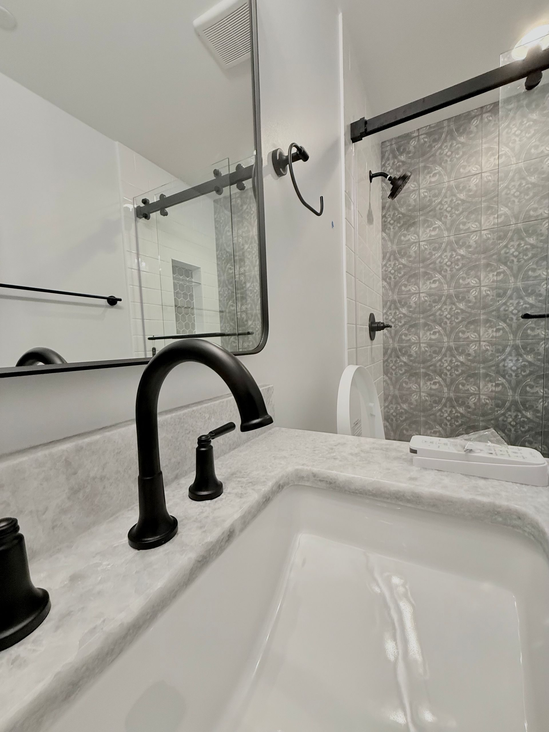 A close-up of the new matte black faucet and sink, showing the reflection of the shower area.