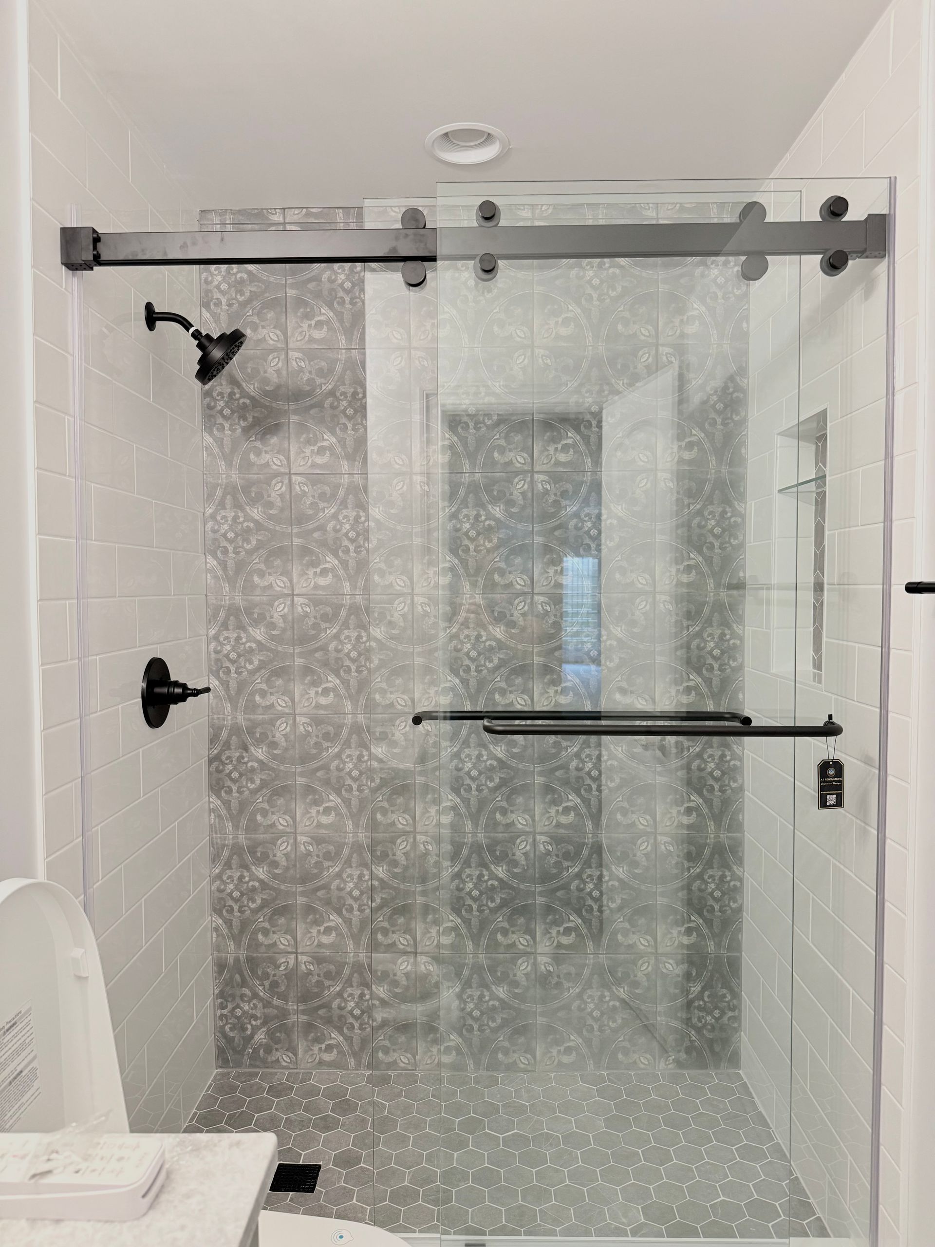 A detail of the new shower conversion with a patterned tile accent wall and hexagon floor tiles.