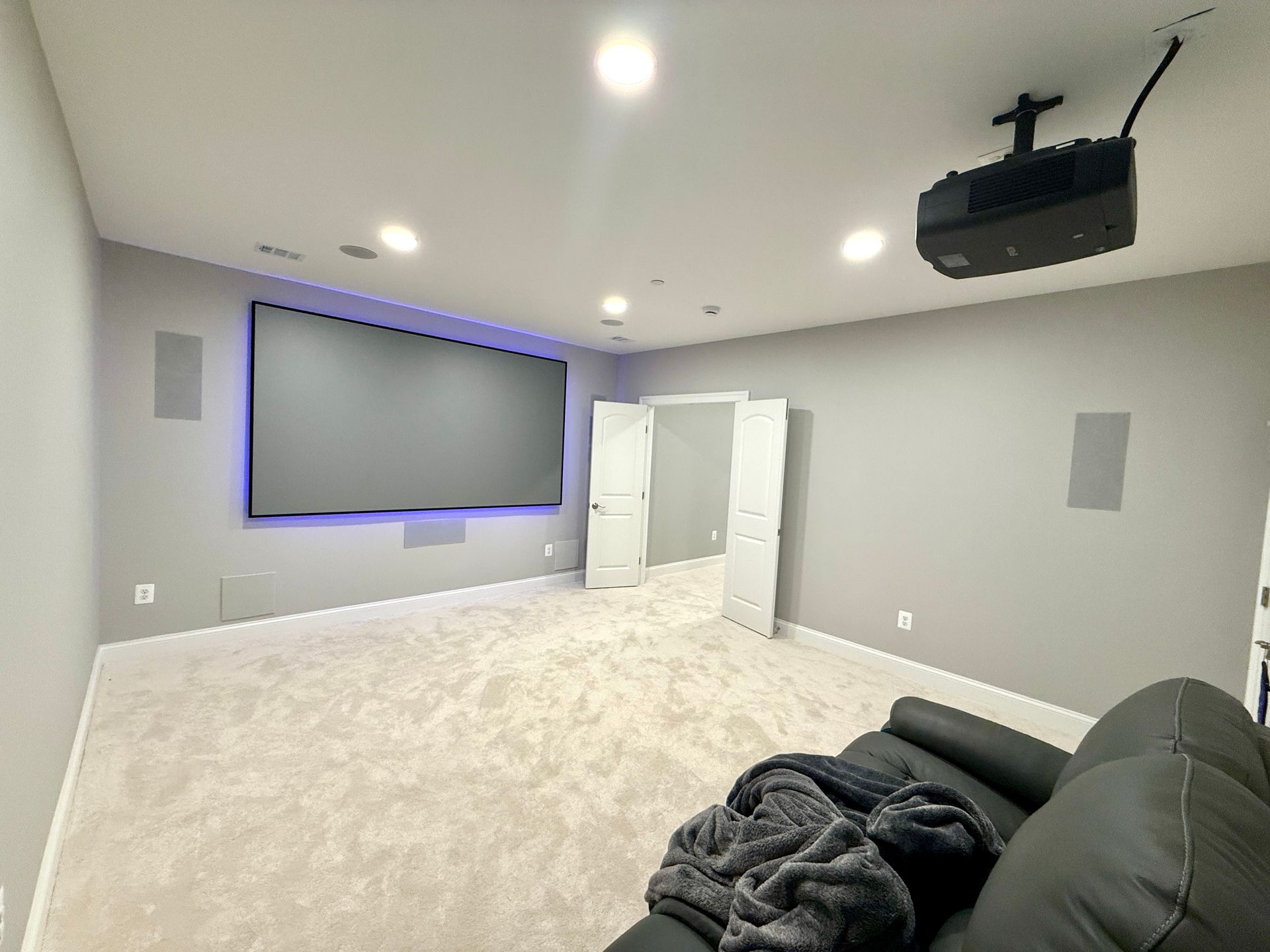 A finished basement cinema room with a large screen, ceiling-mounted projector, and new carpet.