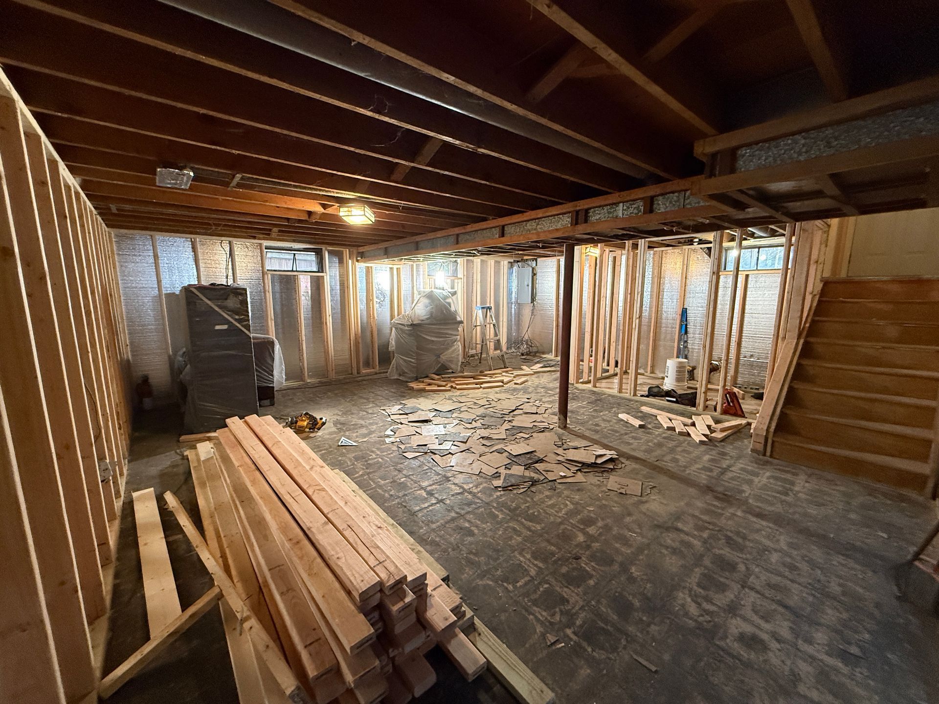 Unfinished Basement Framing: A raw basement interior showing exposed wood framing, silver insulation, and utility pipes before renovation.