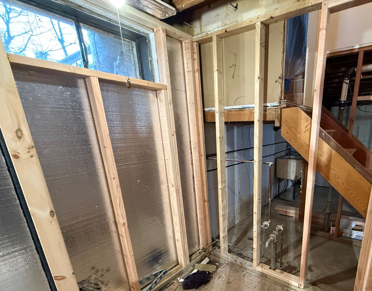 Bathroom Construction Rough-in: An early-stage basement bathroom area showing new wall framing, exposed plumbing pipes, and insulation panels.