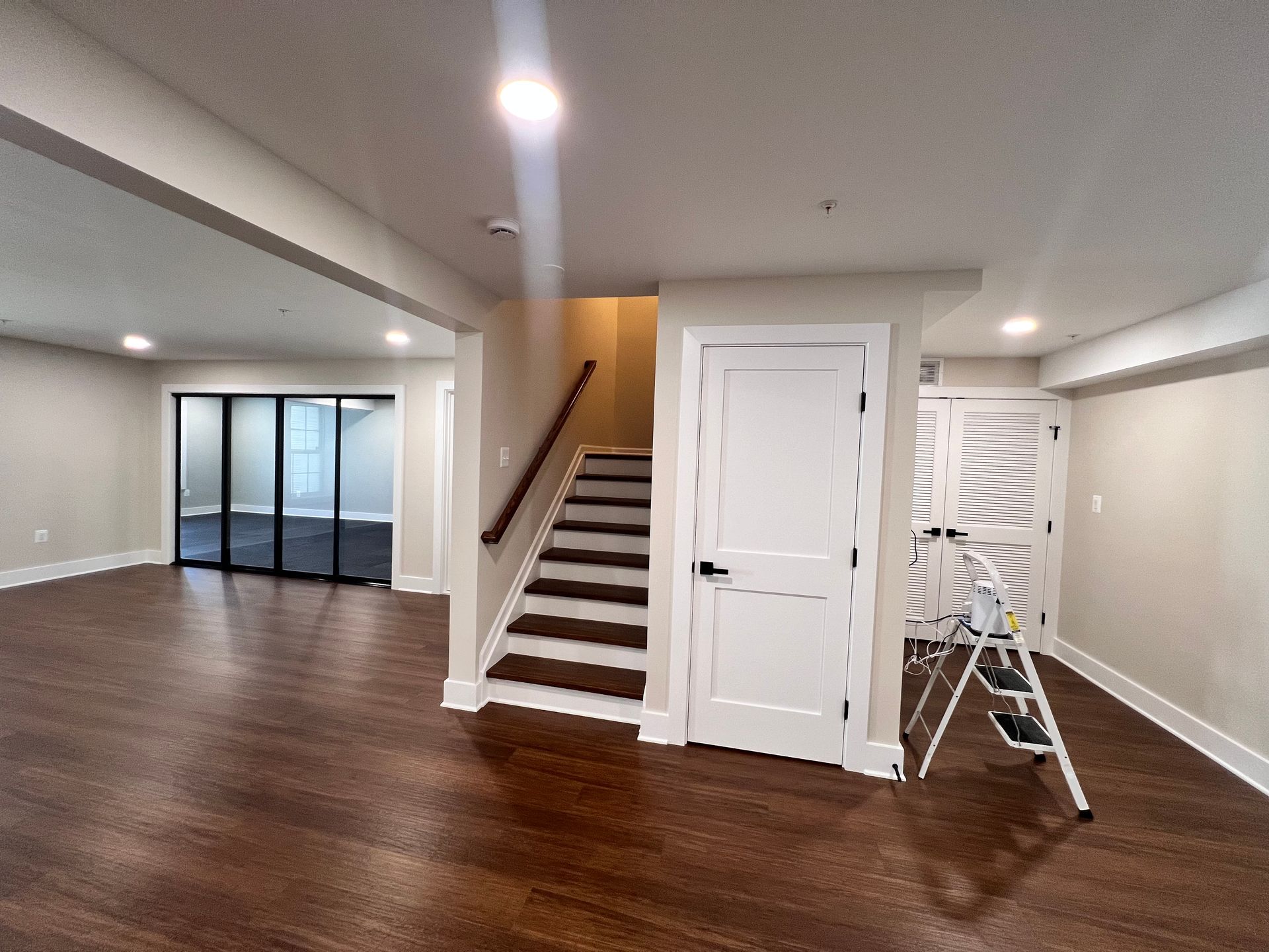 Modern finished basement with a staircase, a closed white door, dark LVP floors in Greater Baltimore, MD