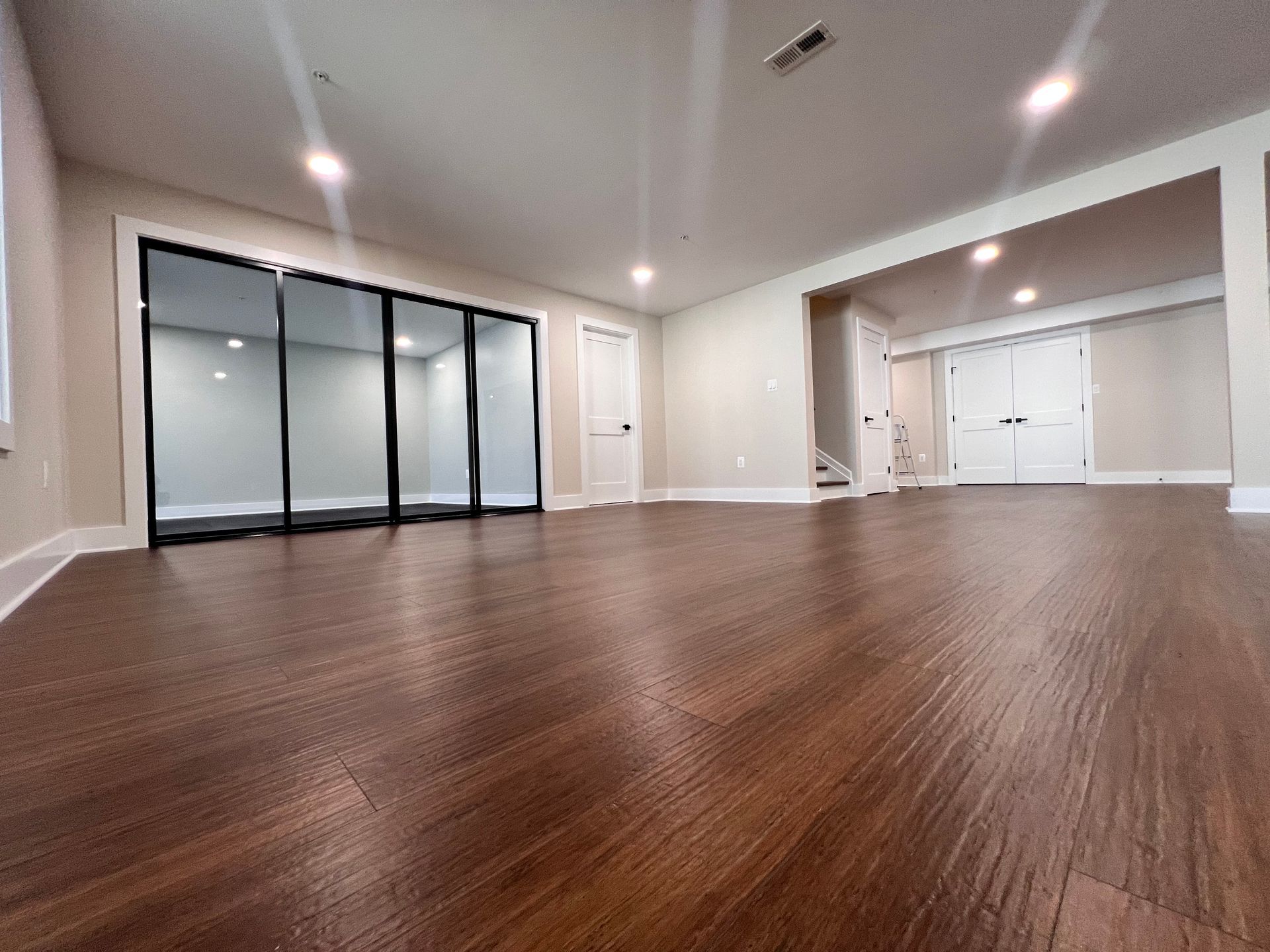 Finished basement with sliding glass doors, white doors, and dark wood-look floors.