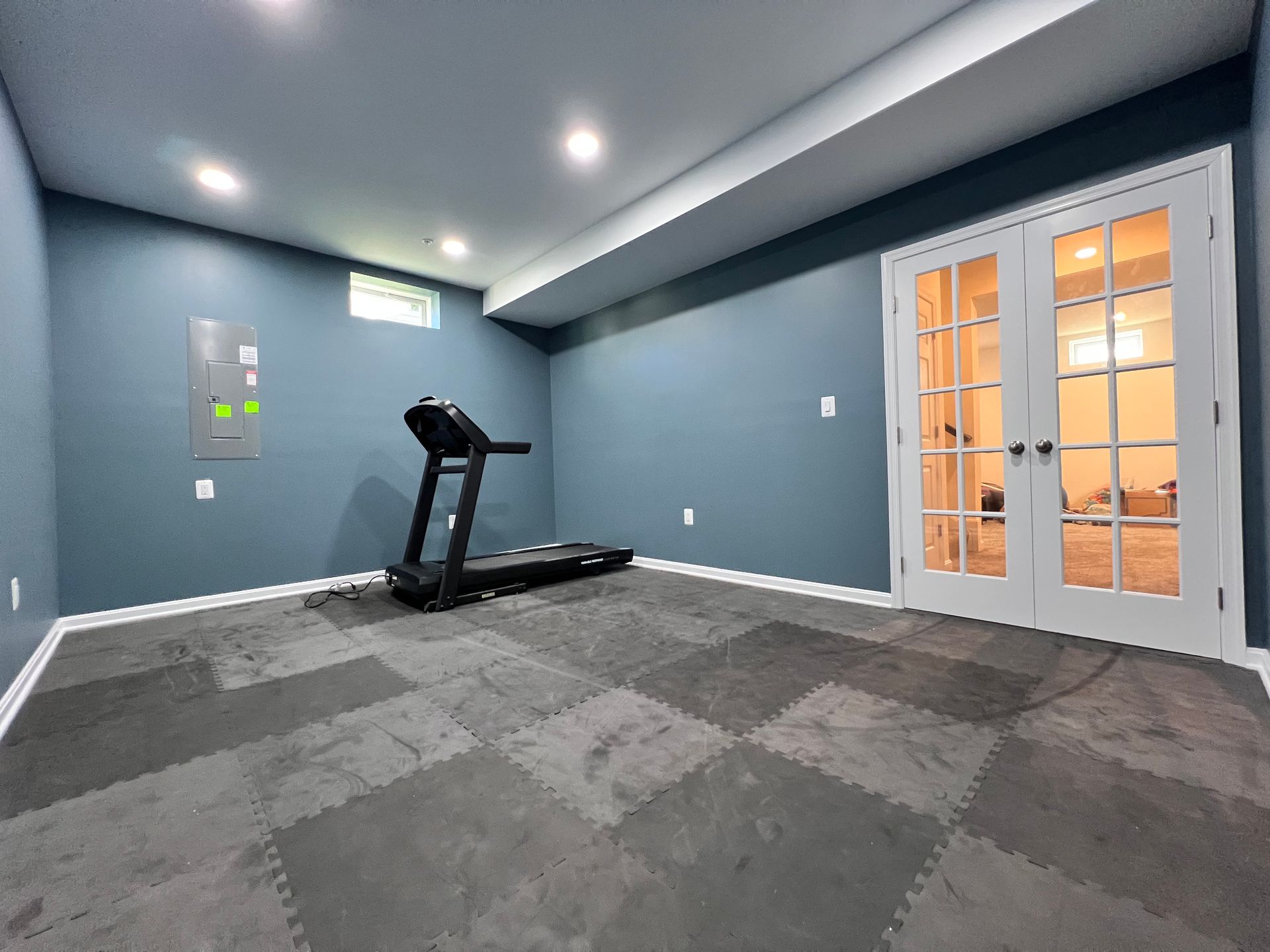 Finished basement gym with treadmill, blue walls, and glass doors in Greater Baltimore, MD