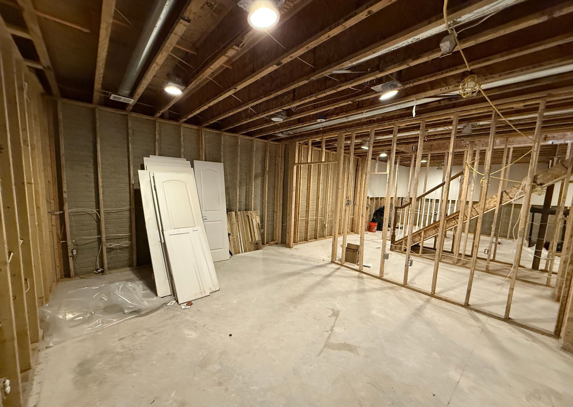 A raw, unfinished basement showing a concrete floor and framed walls before a full remodel.