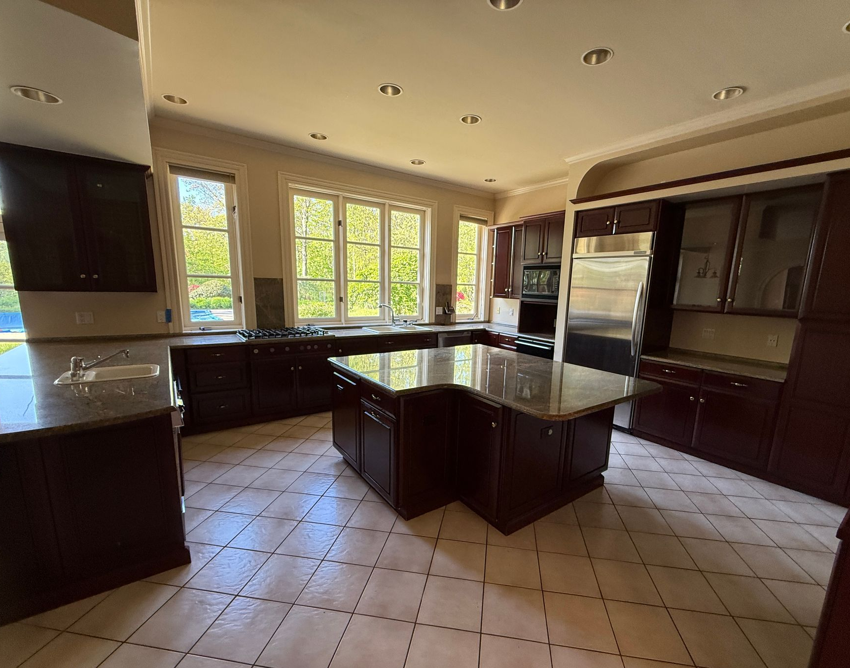 A spacious, modern kitchen with a large navy blue island, white granite countertops, and elegant gold pendant lights.