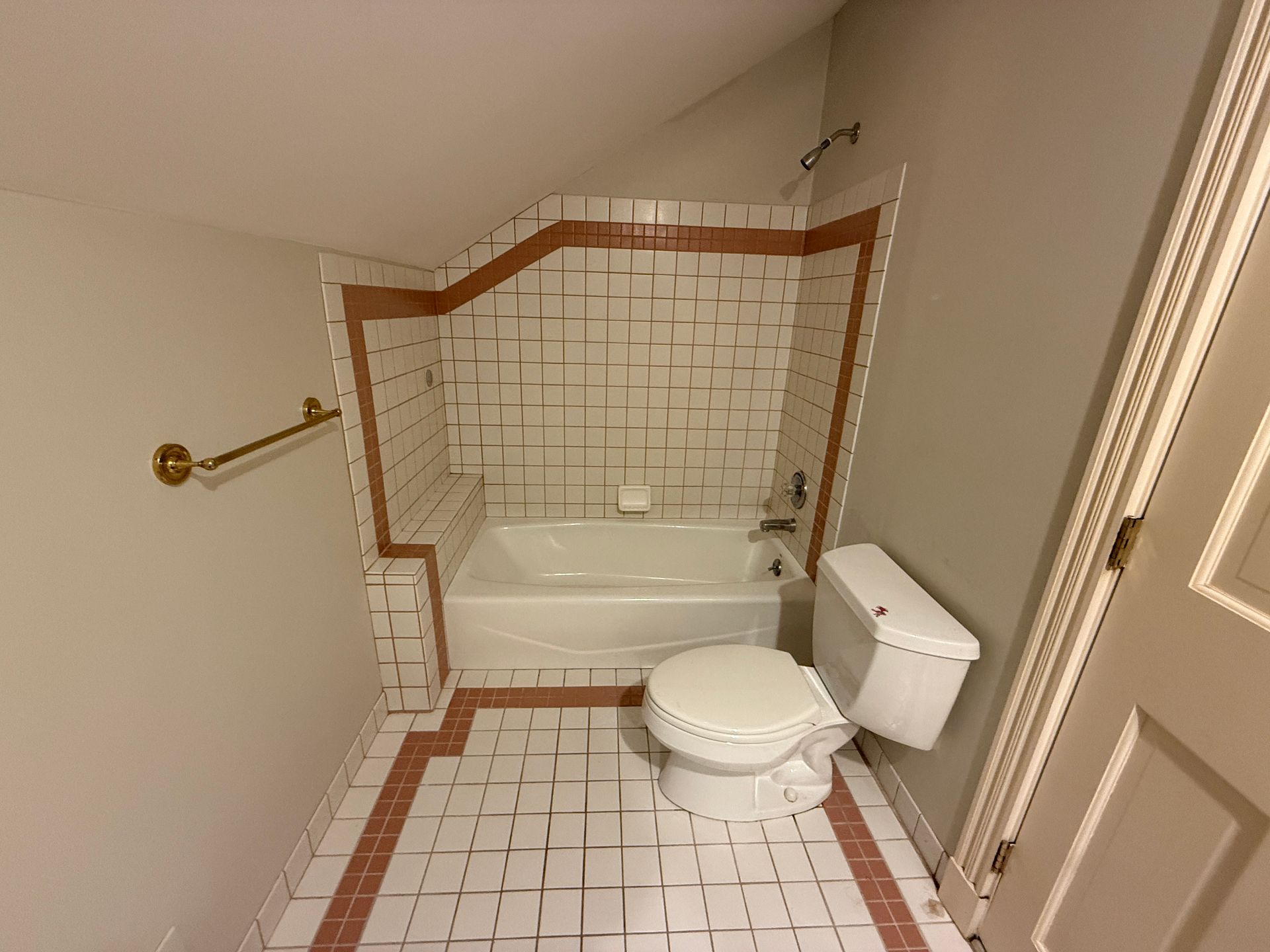  A cramped bathroom space before renovation, showing a small tub and outdated tile.