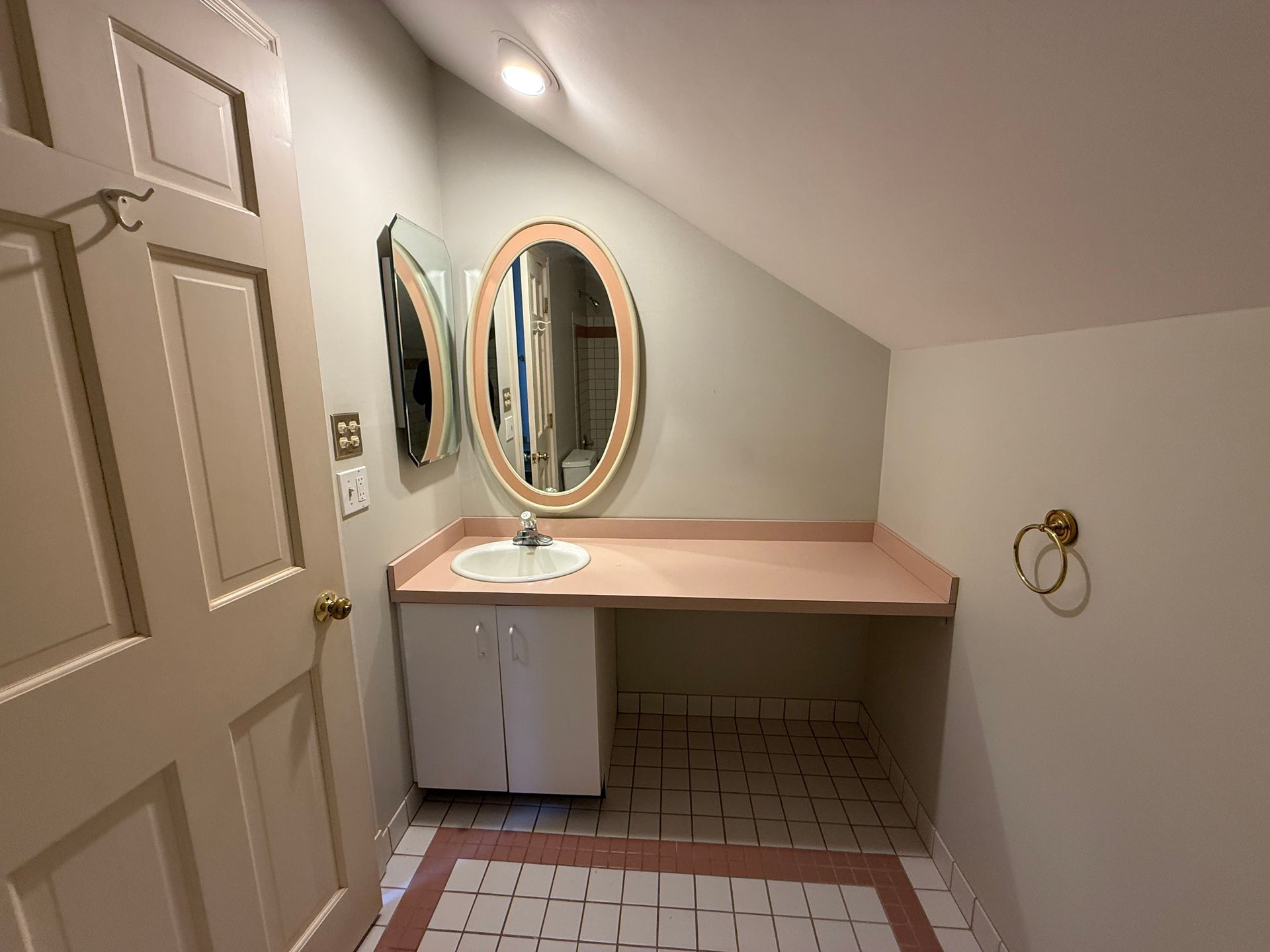 A pre-renovation shot of the bathroom sink and mirror area with pink countertops and an old vanity.