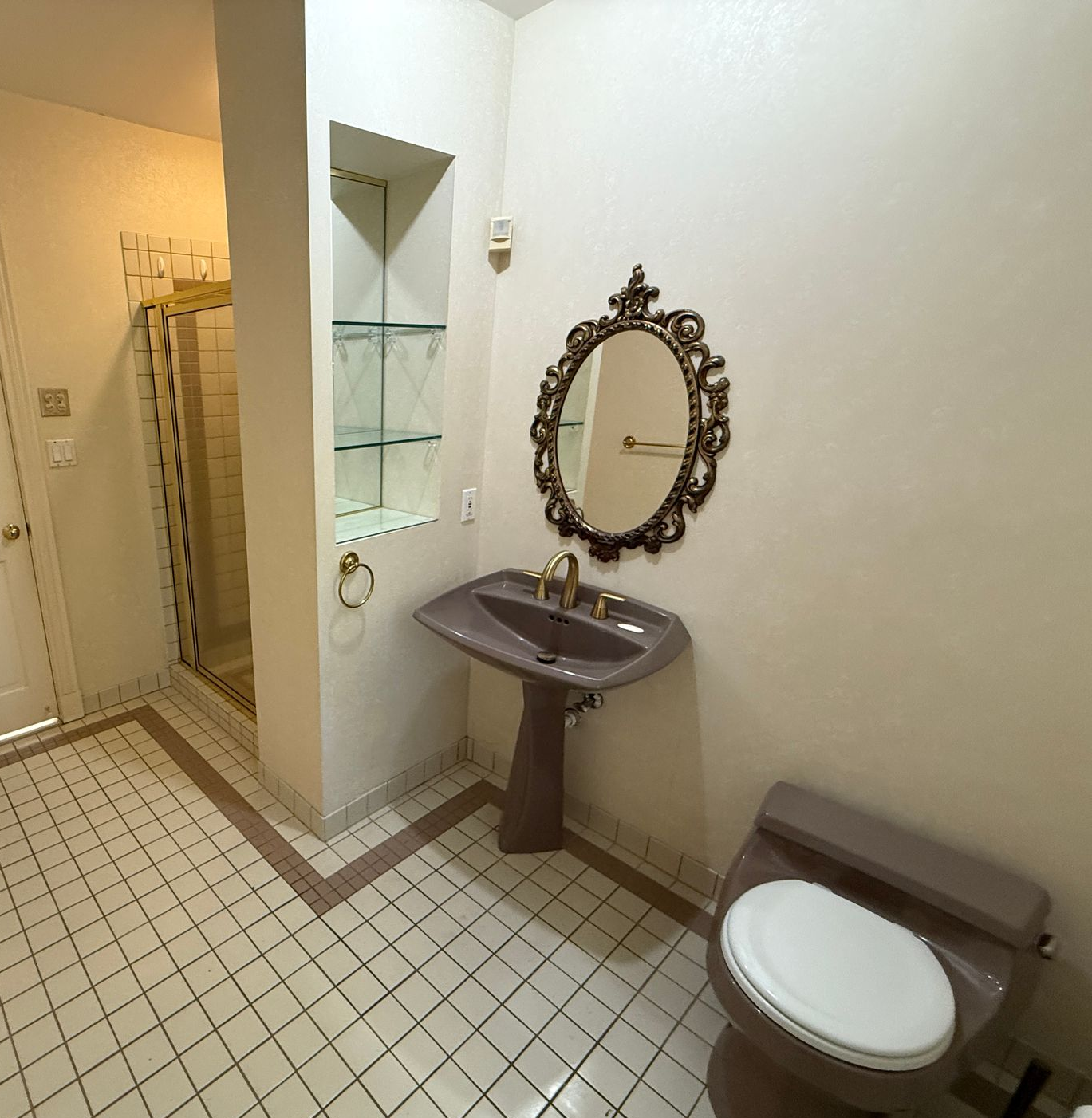 A vintage bathroom with a pink toilet and gold-framed shower.