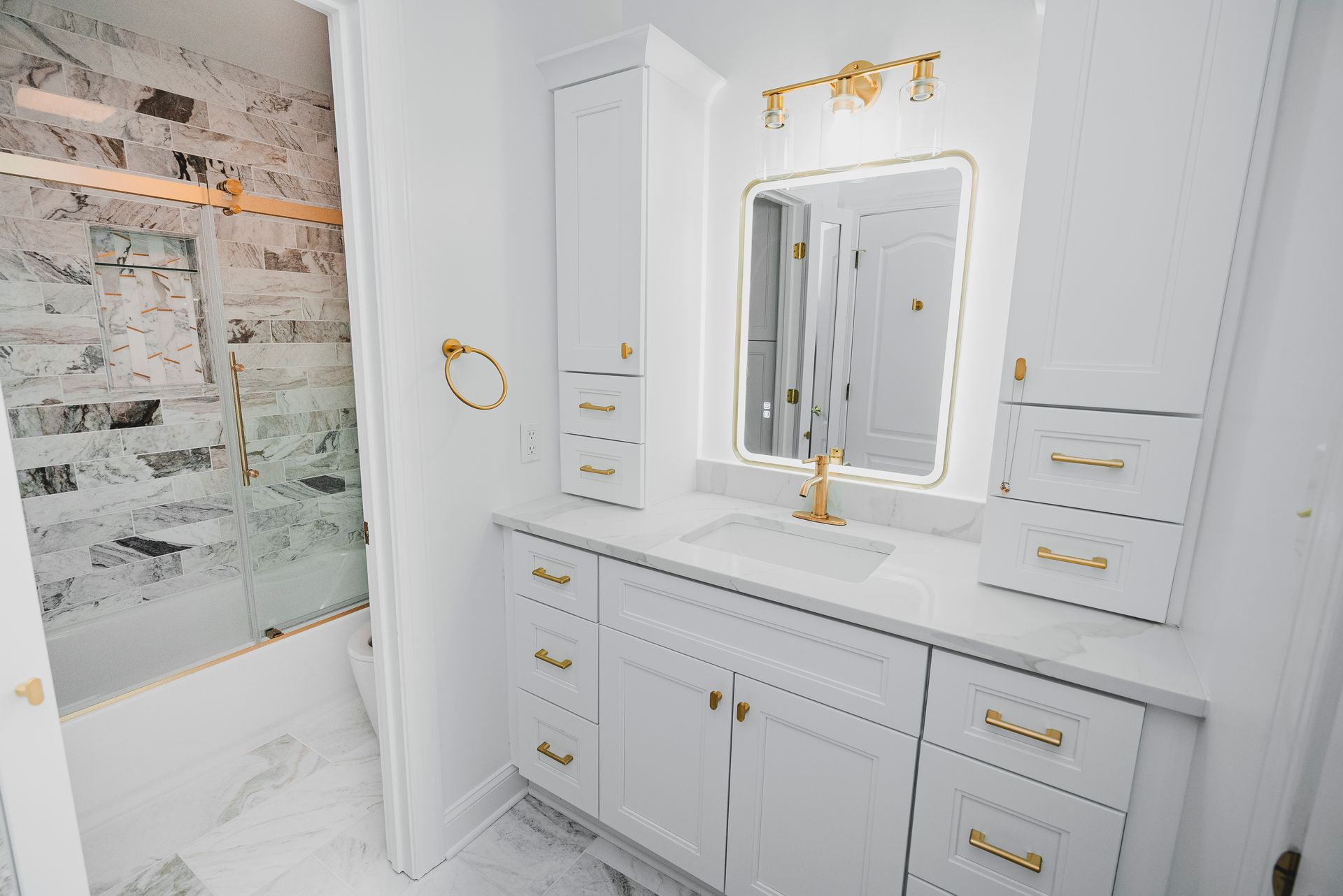 Luxury gold and white bathroom design with a custom marble-style tile shower and sliding glass door.