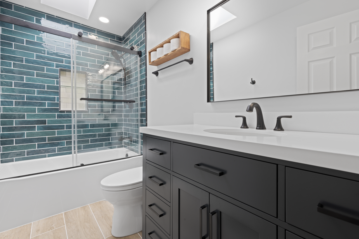 Newly remodeled bathroom showcasing bold teal tile, a dark vanity, and light wood-look floor tiles.