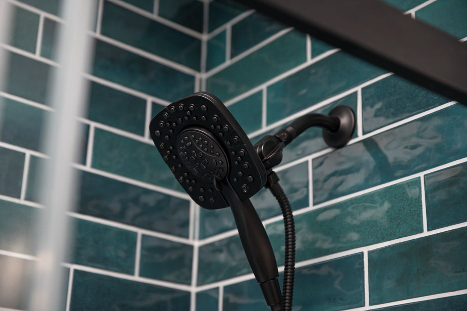 Matte black showerhead and hand shower against vibrant teal subway tile.