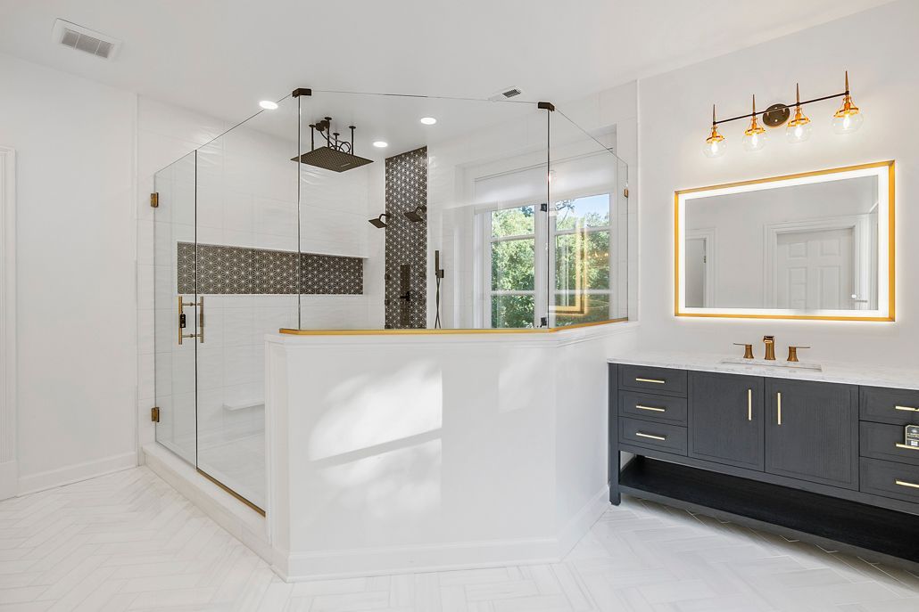 Primary Suite Shower Remodel in Towson, MD with gold-trimmed glass enclosure, modern black vanity, and bright white herringbone floors.