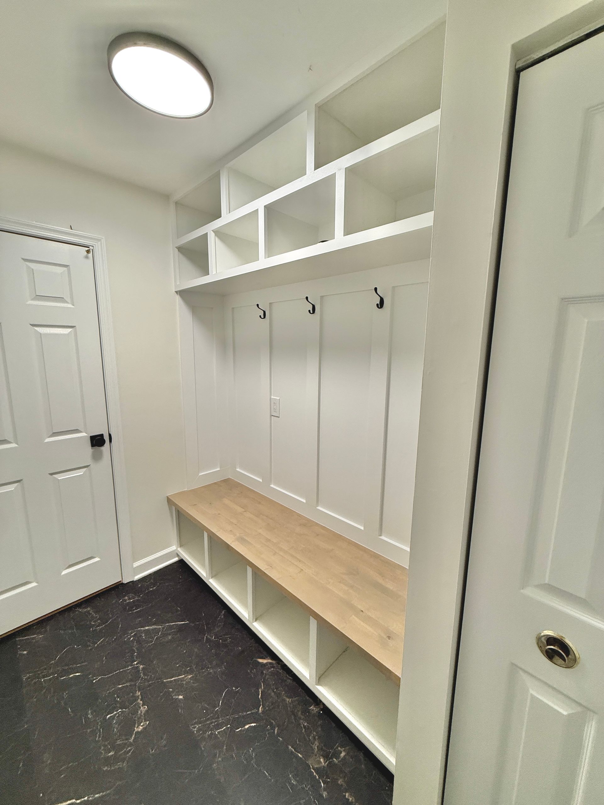 Custom built-in mudroom cabinetry near entryway, featuring natural wood bench and overhead shelving.