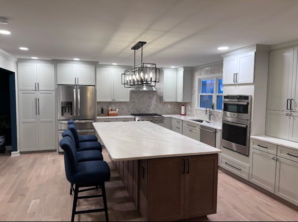 Spacious kitchen remodeling with light gray cabinets, a contrasting wood-toned island, blue barstools, and modern light fixtures in Eldersburg, MD