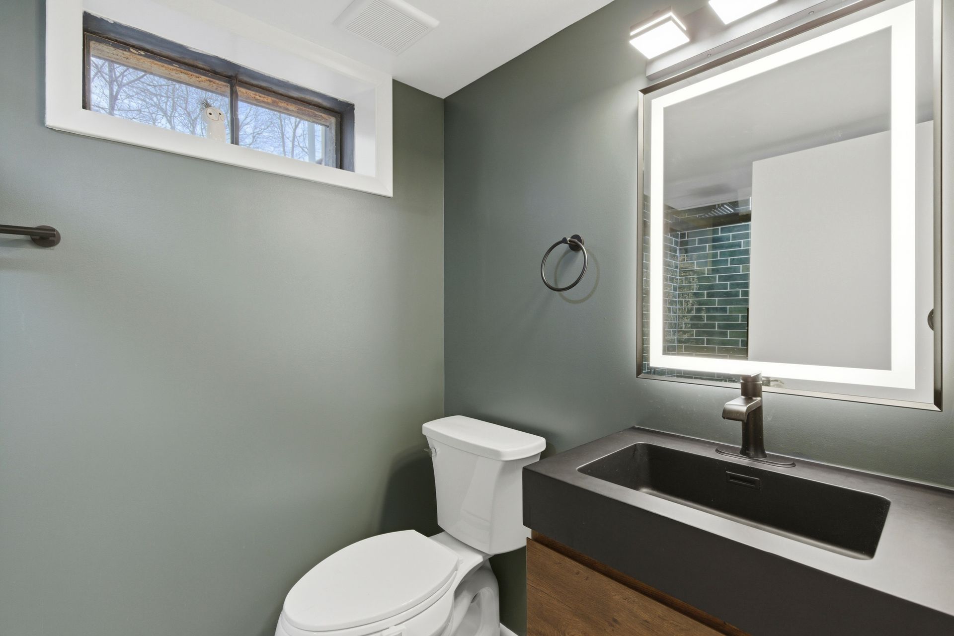 Luxury Walk-in Shower: The completed basement bathroom showcasing textured green subway tile, sleek matte black fixtures, and a glass partition.