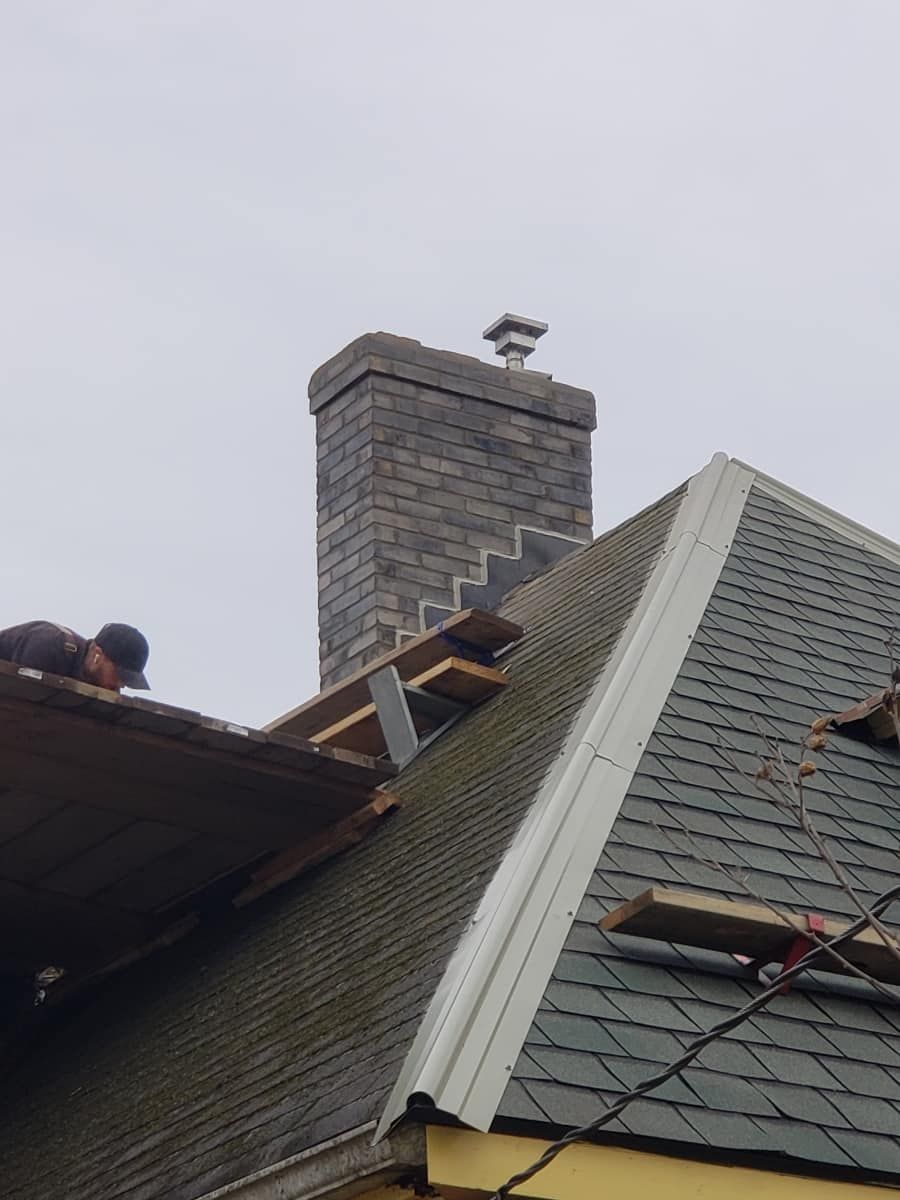 Roof with missing shingles near a brick chimney.