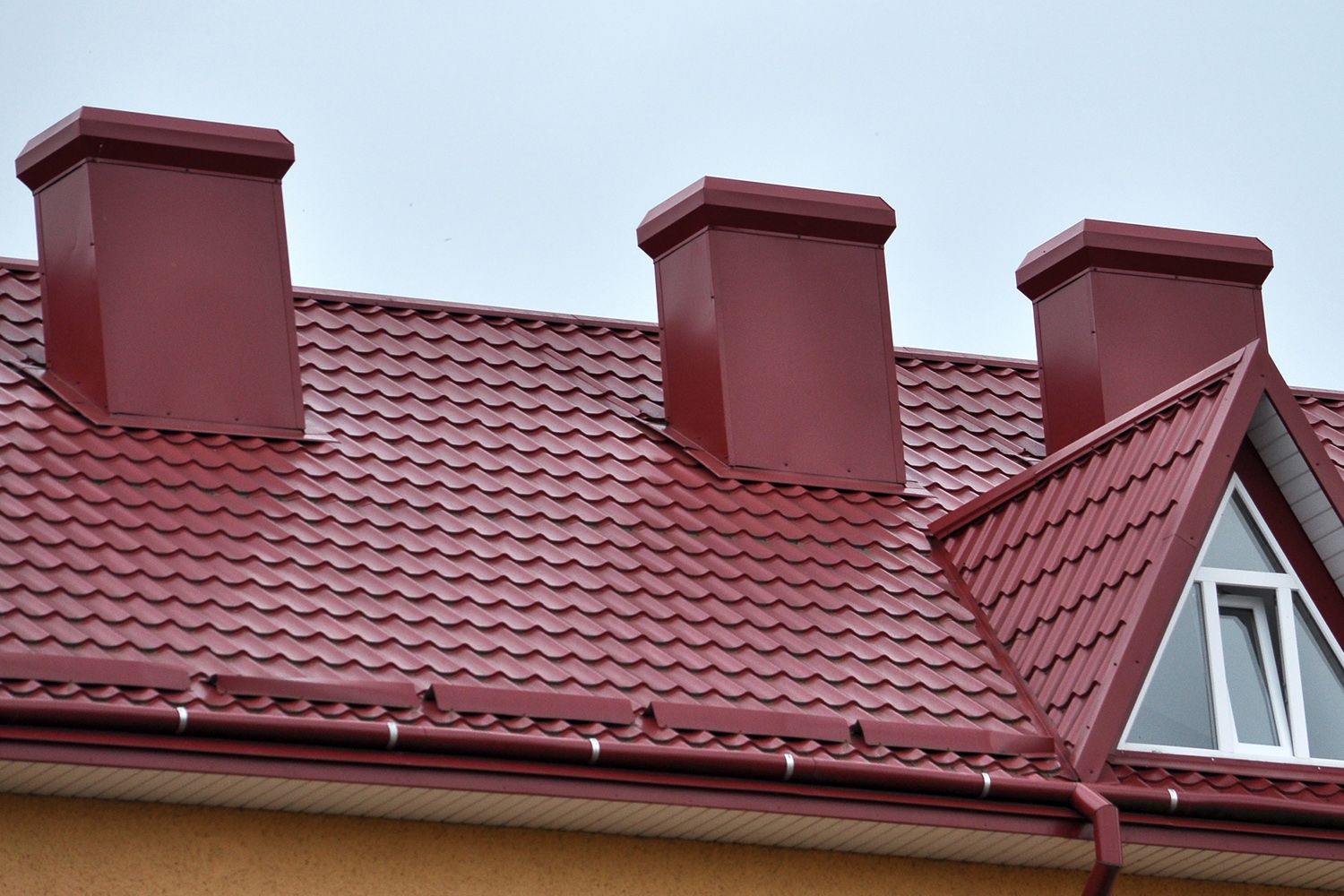 Red metal roof with three matching chimneys and a dormer window.