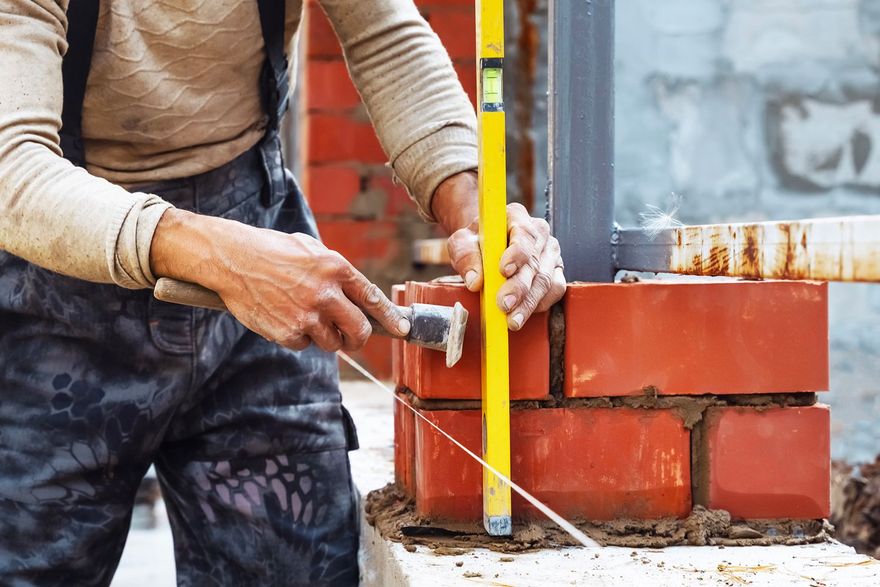 A bricklayer uses a level and hammer to build a brick structure, outdoors, during the day. A bricklayer uses a level and hammer to build a brick structure, outdoors, during the day.