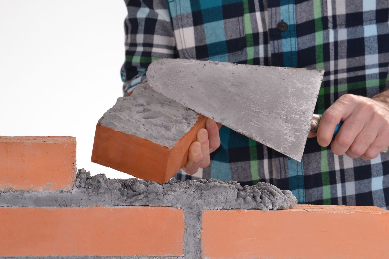 Person laying brick with a trowel, applying mortar, building a wall.