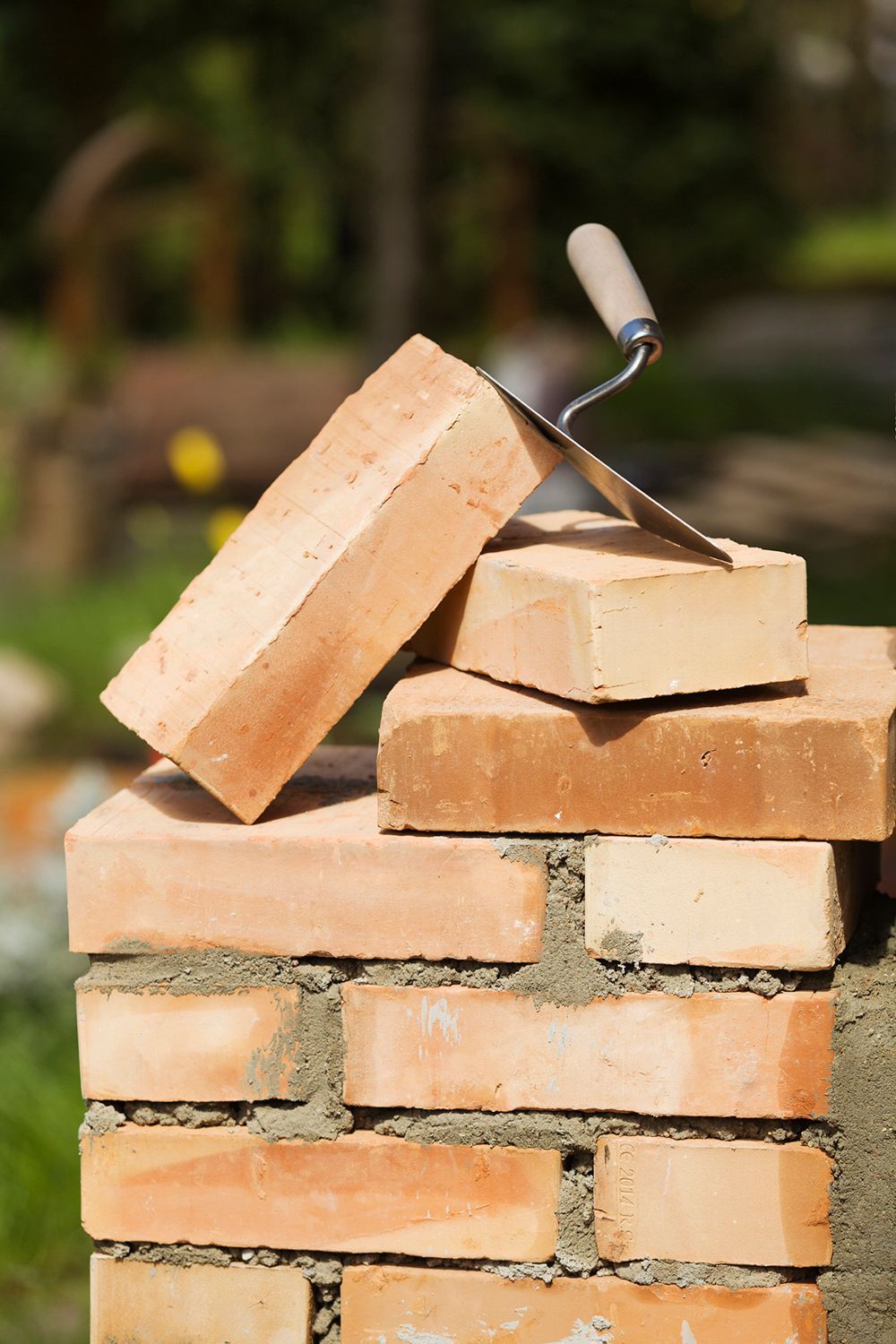 Bricks stacked to form a wall with a trowel on top, outdoors, natural light.