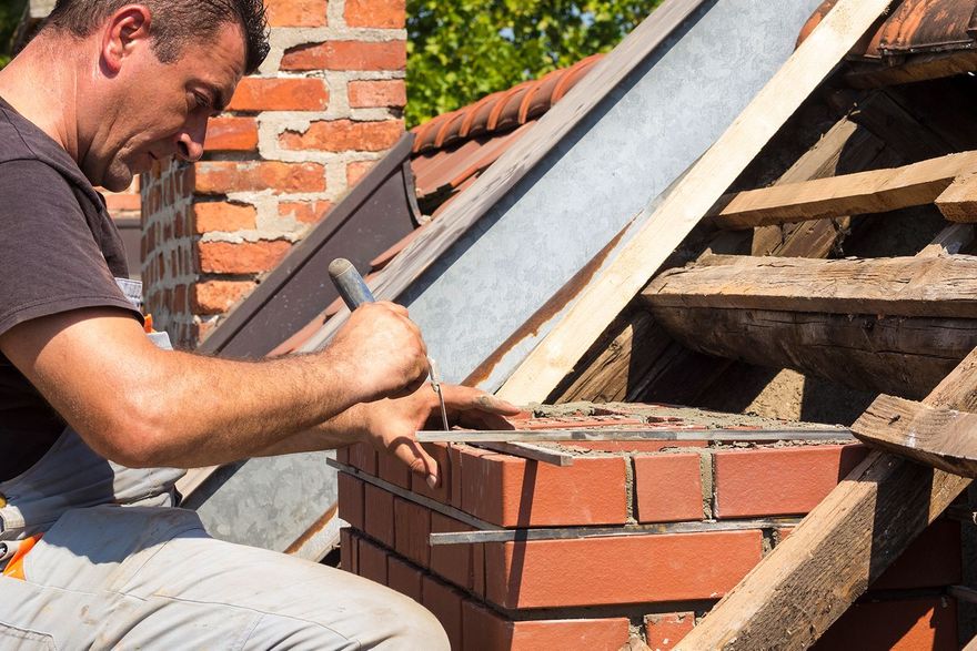 Man building a brick chimney on a rooftop, using a hammer and metal measuring tools. Man building a brick chimney on a rooftop, using a hammer and metal measuring tools.