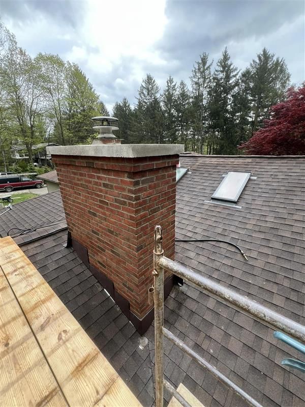 Red tiled roof with three brick chimneys against a clear blue sky.