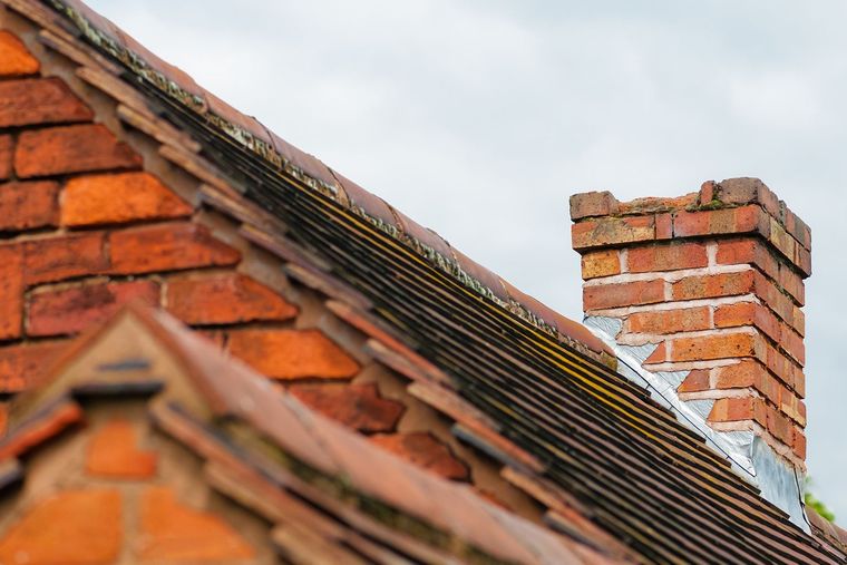 Red brick roof with chimney against a cloudy sky. Red brick roof with chimney against a cloudy sky.
