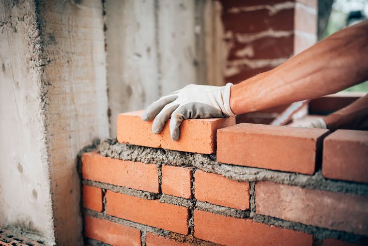 Mason wearing gloves laying red bricks with mortar. Mason wearing gloves laying red bricks with mortar.