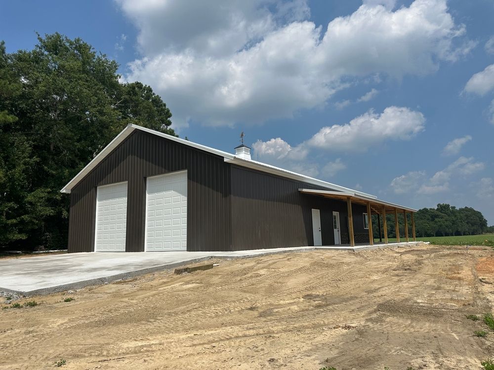 A large building with two garage doors is sitting in the middle of a dirt field.
