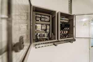Open electrical control cabinets mounted on a white wall containing various circuit breakers and wiring components.