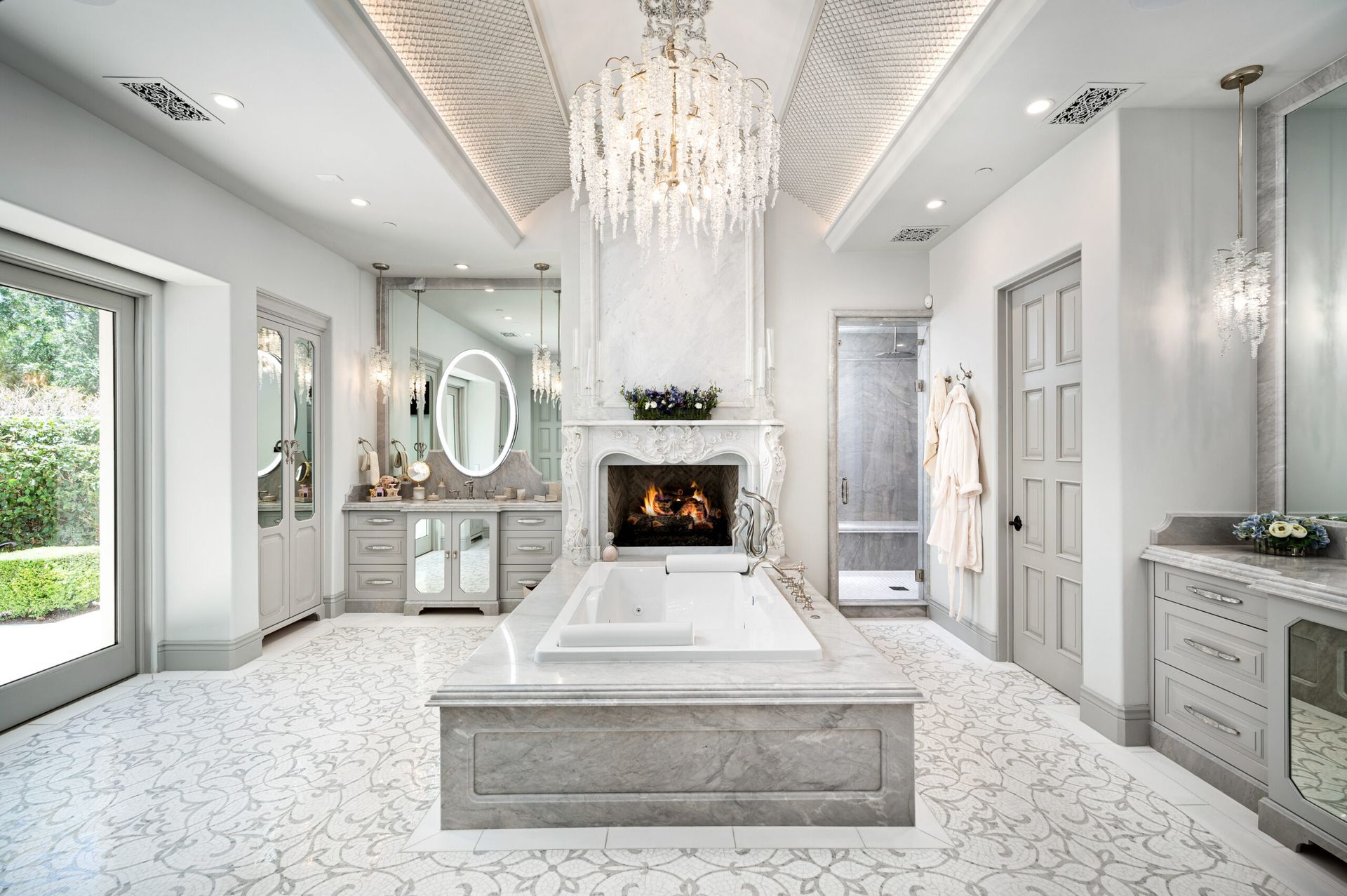 A bathroom with a large tub , fireplace , mirror and chandelier.