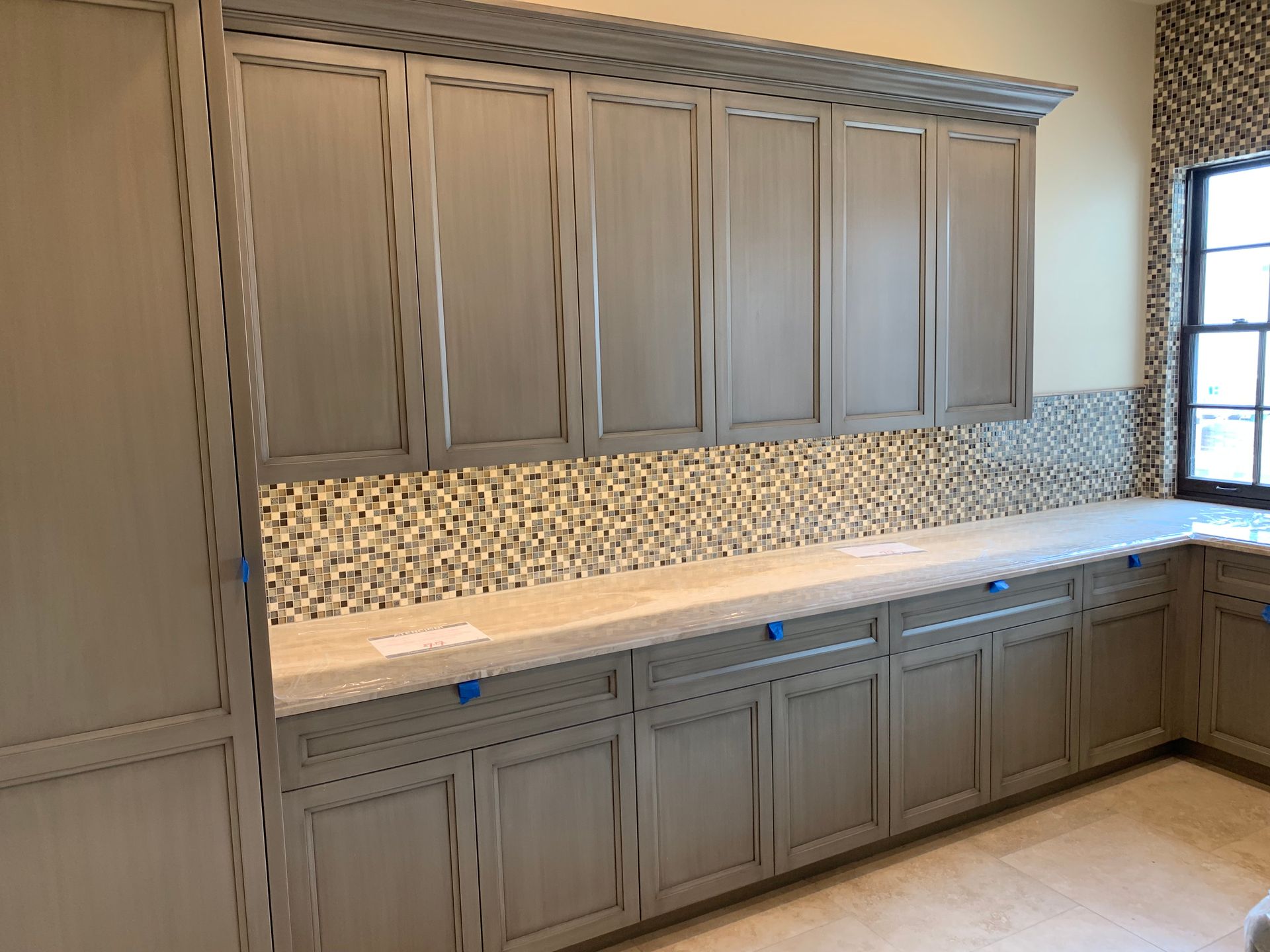 A kitchen with gray cabinets and white counter tops.
