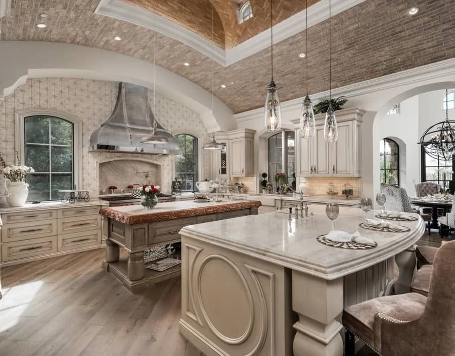 Spacious kitchen with brick-patterned ceiling, two islands, and large windows. Light wood floors and cream-colored cabinets.