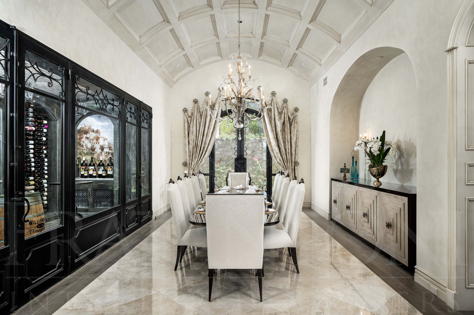 A formal French style, dining room, custom white chairs, a coffered ceiling, and a glass-walled wine cellar.