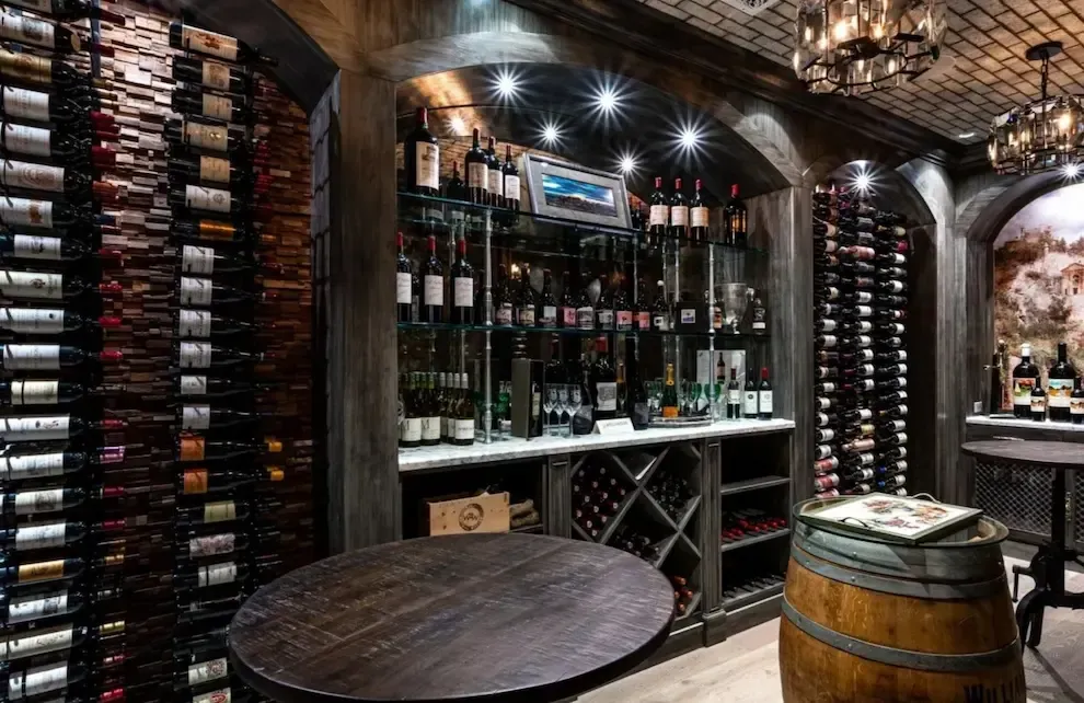 Wine cellar with arched alcoves, dark wood wine racks, a barrel, and a table.