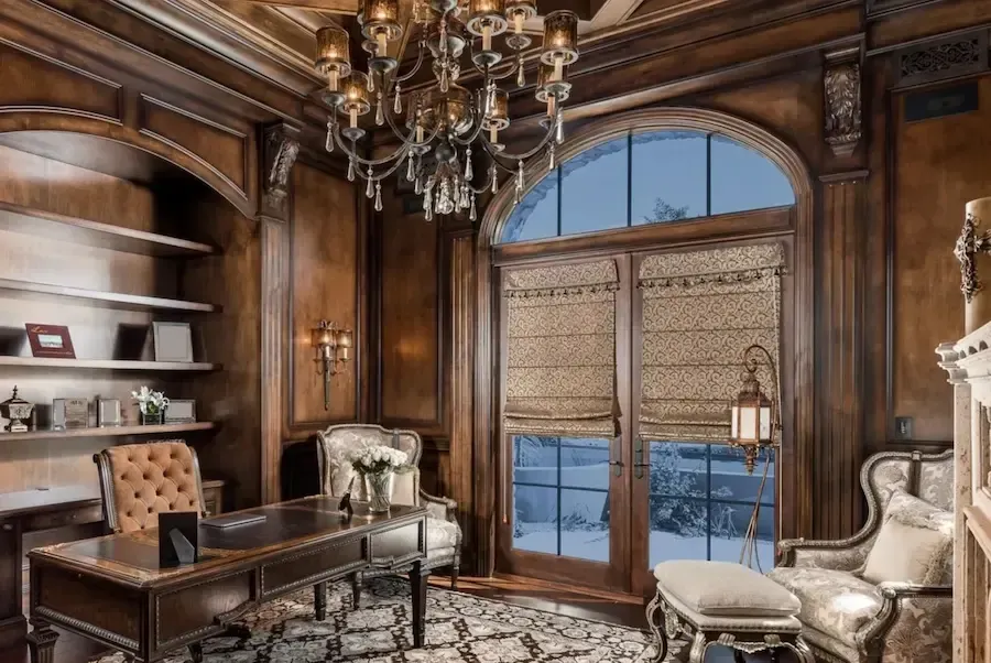 Ornate wood-paneled study with desk, bookshelf, and chandelier. Large arched window with view, patterned rug.