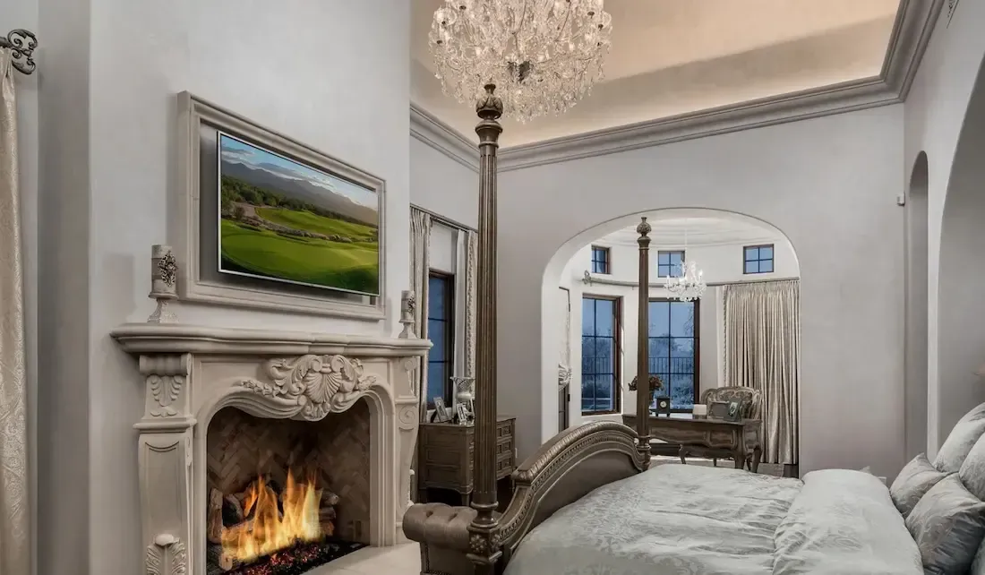 Luxurious bedroom with fireplace, chandelier, and a view through an arched doorway.