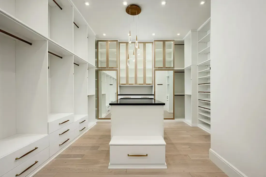 modern custom walk-in closet with white drawers, gold mirrored cabinets, wood floors and a chandelier