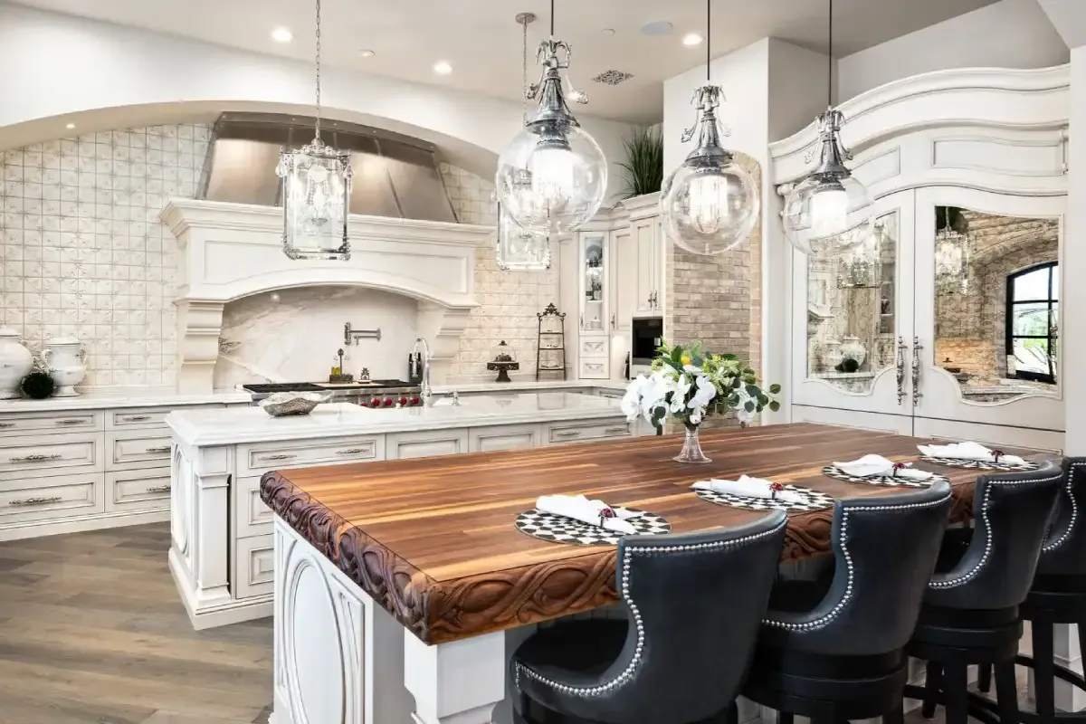 Elegant bedroom with chandelier, arched ceiling, bed, fireplace, and balcony access. Beige and white tones.