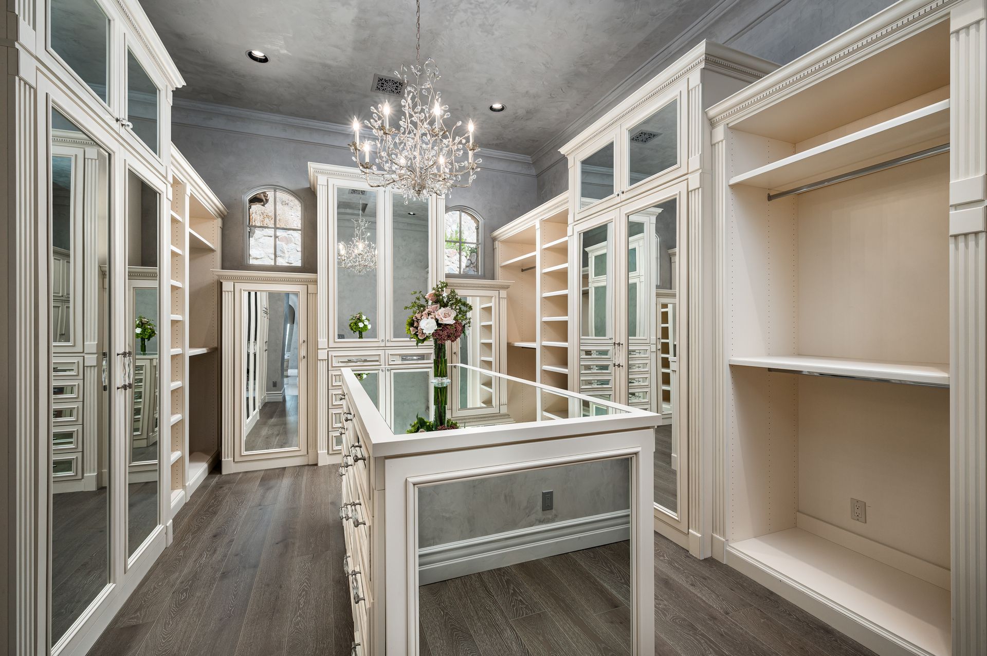 luxury walk-in closet with white mirrored cabinets, wood floor, and chandelier