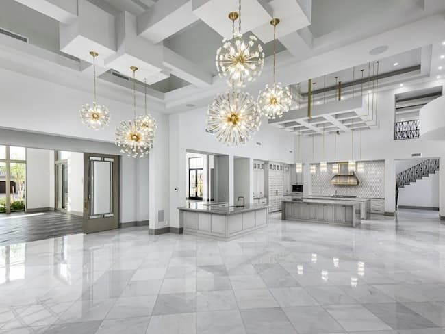 A large empty room with a kitchen and chandeliers hanging from the ceiling.