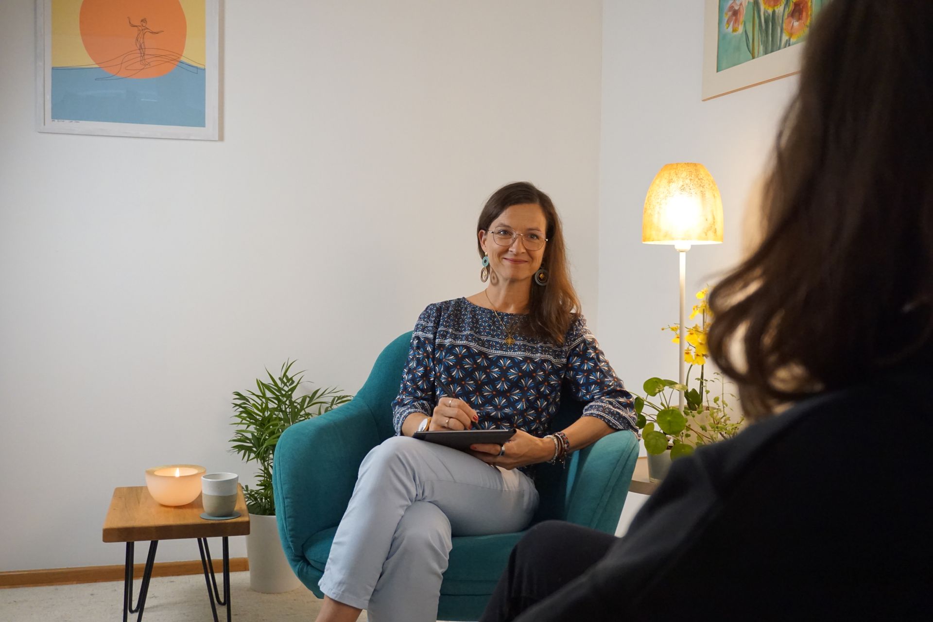 Frau auf türkisfarbenem Stuhl, lächelnd, macht sich während einer Beratungssitzung Notizen.