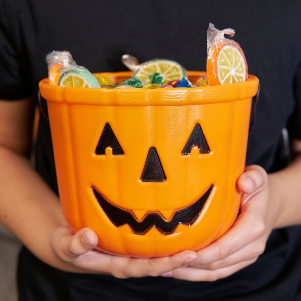 A person is holding an orange pumpkin bucket filled with candy.