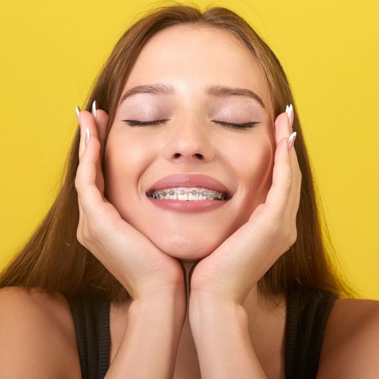 A woman with braces on her teeth is smiling with her eyes closed.