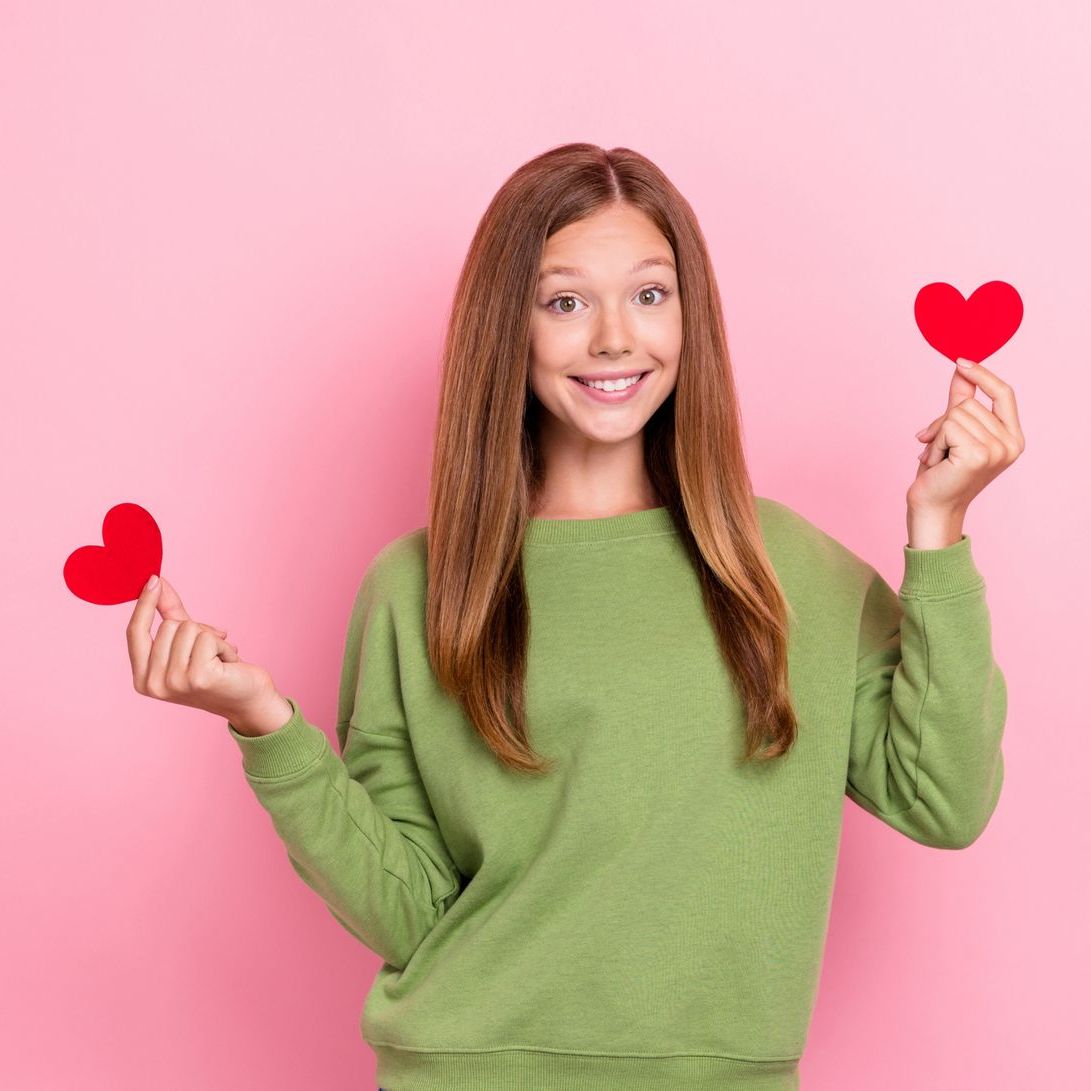 A woman in a green sweater is holding two red hearts in her hands.