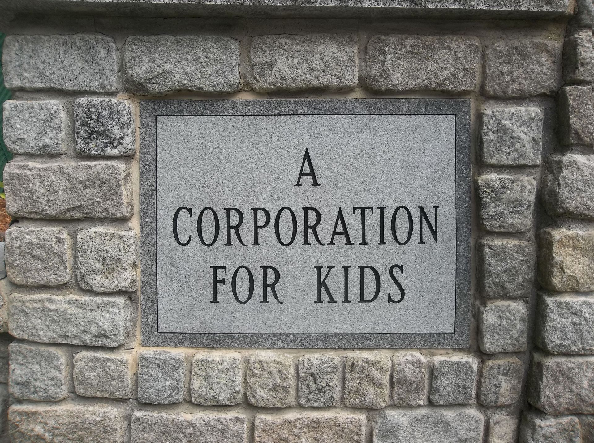 A sign on a brick wall that says a corporation for kids