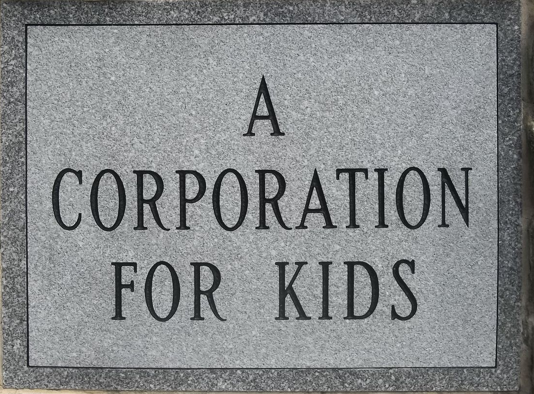 A sign on a brick wall that says a corporation for kids